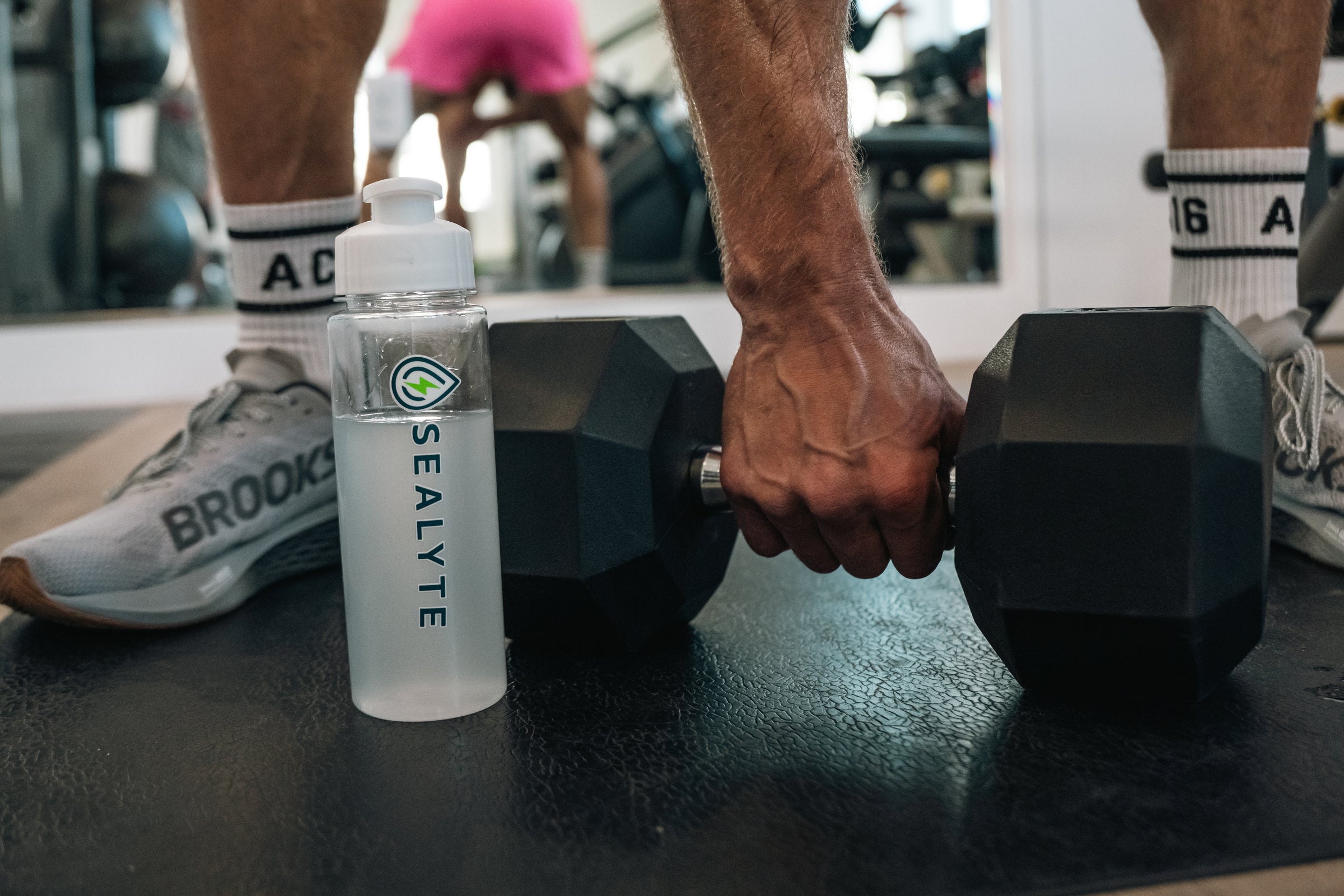Sealyte hydration bottle beside a heavy dumbbell during gym workout – ideal for electrolyte replenishment and athletic performance support.